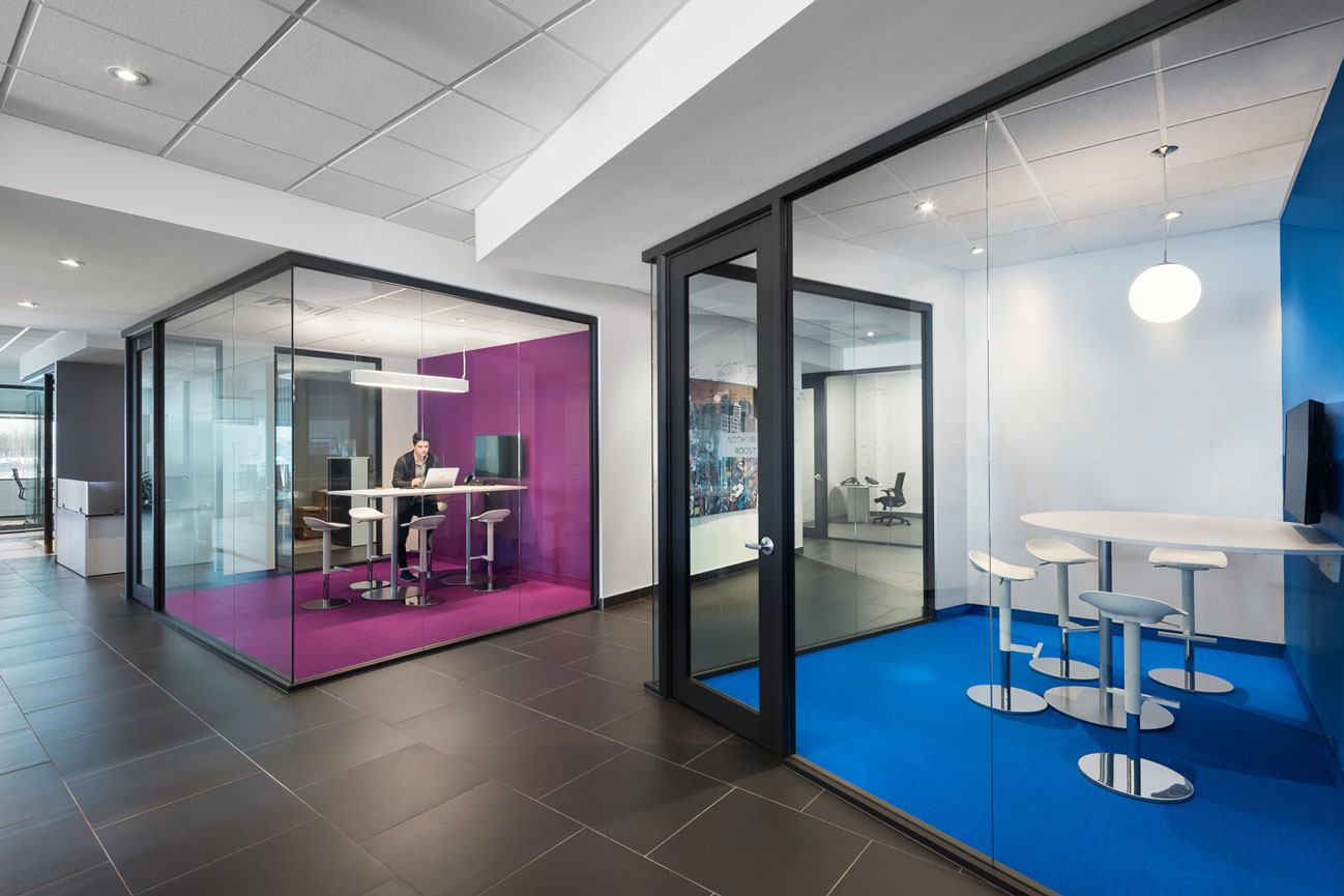 View of Medicom offices showing 2 glass box meeting rooms, one blue and one purple with an employee working on a laptop..