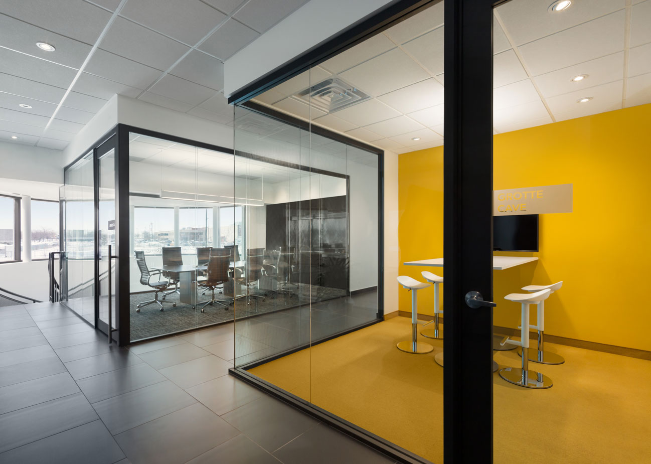 Glass cube meeting room with yellow floor and wall and formal neutral colored meeting room in background.